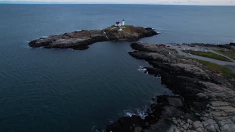 Swooping-angle-of-lighthouse-on-a-rocky-island-with-water-crashing-on-the-rocks-and-blue-water-rippling