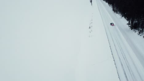 Das-Elektroauto-Fährt-Auf-Einer-Schneebedeckten-Straße-Mit-Einem-Wunderschönen-Blick-Auf-Die-Berge-Am-Polarkreis-Von-Der-Drohne-Aus