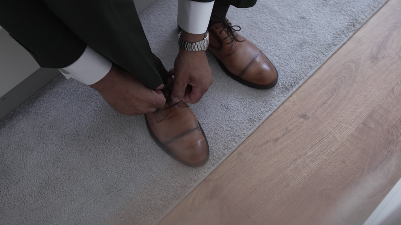 Man in formal attire tying brown leather dress shoes while sitting indoors