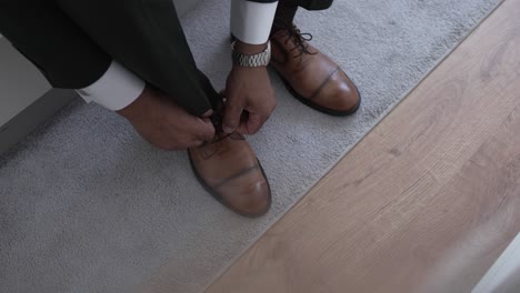 man in formal attire tying brown leather dress shoes while sitting indoors