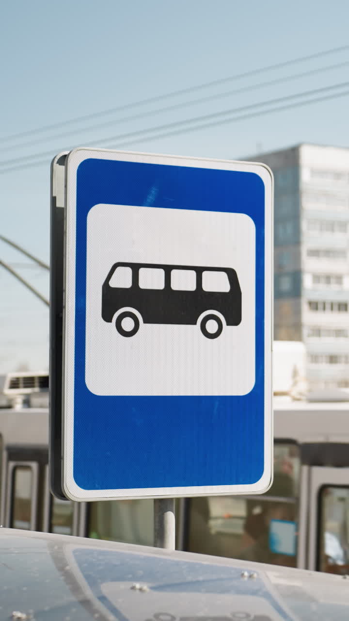 버스와 건물을 배경으로 한 도시 환경에서 버스 정류장 표지판의 근접 시각, 자동차와 버스가 움직이고 있습니다.