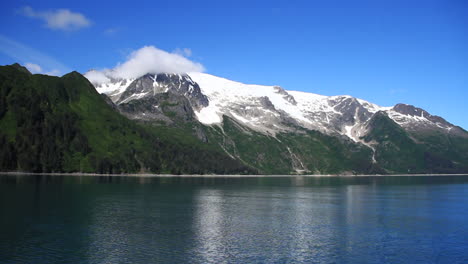 beautiful blue ocean passes by in front of snow covered mountains and clouds