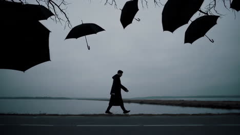 surreal scene of a lone man walking beside a lake with floating umbrellas and bare tree branches