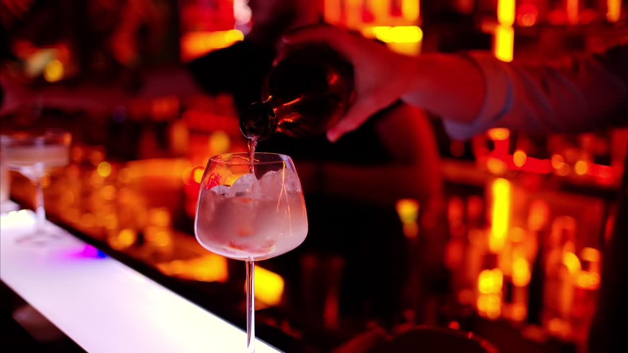 Barman making a cocktail with white sparkling wine at the bar at night with red neon lights, slow motion