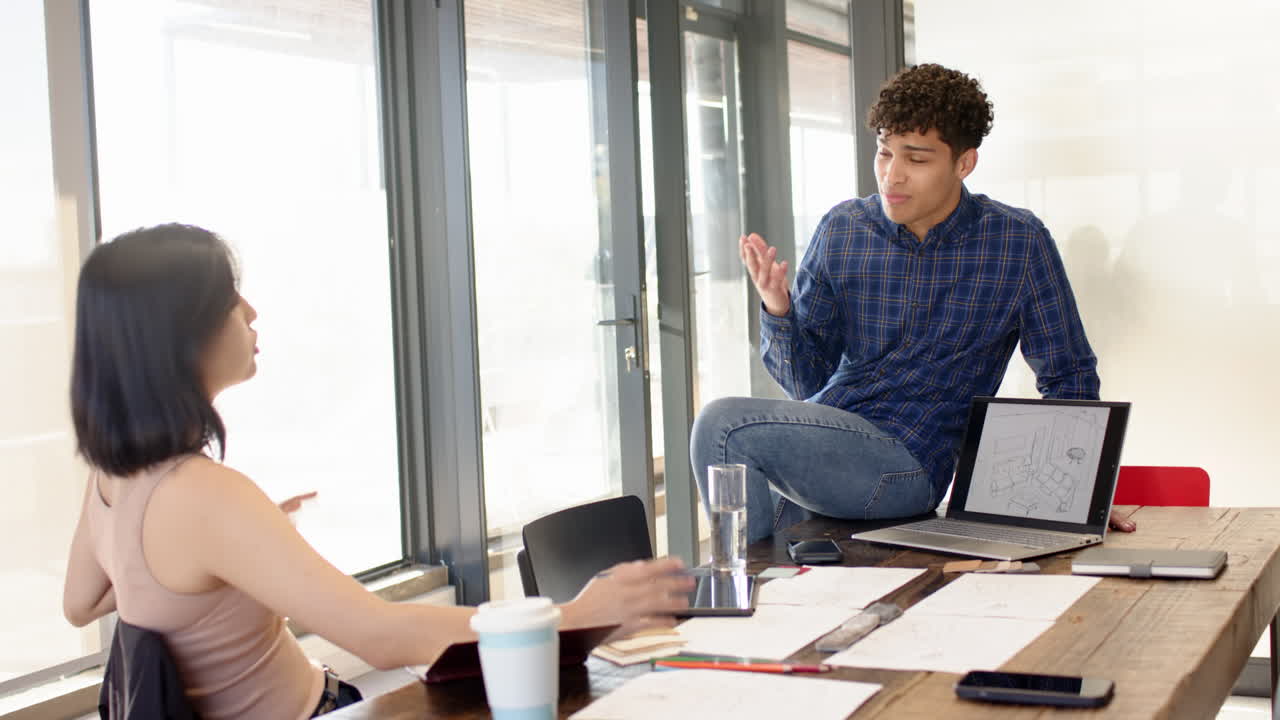 Discussing interior design plans, multiracial colleagues using laptop and blueprints in office