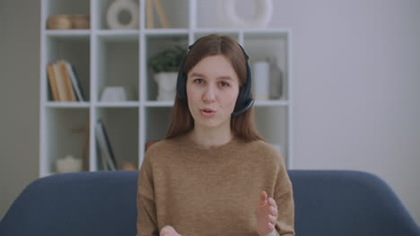 portrait of online consultant woman with headphones on head sitting at table and talking to camera