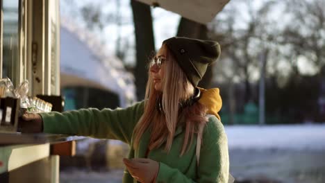 Woman-considers-gingerbread,-taking-a-hot-coffee-in-street-kiosk-on-winter-walk