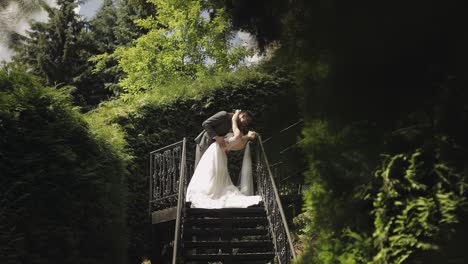 Newlyweds,-caucasian-groom-with-bride-stay-on-stairs-in-park,-wedding-couple,-man-and-woman-in-love