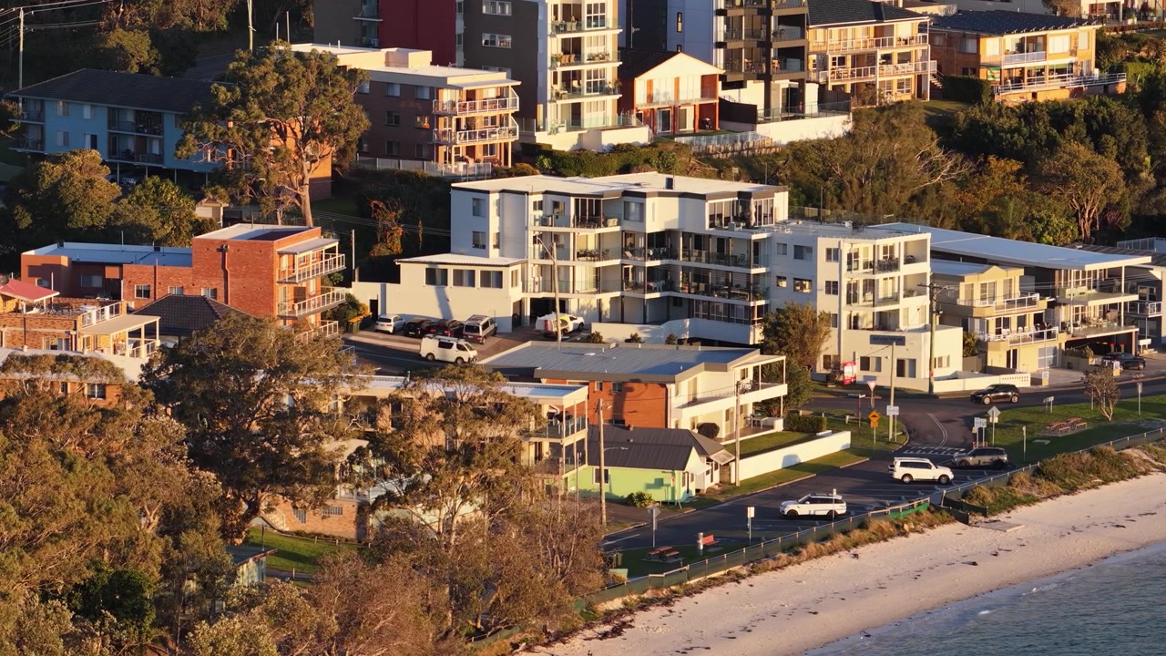 Fugleperspektiv af kystlejligheder og strand under den gyldne time i Nelson Bay, Australien.