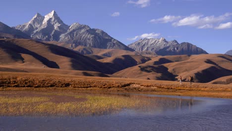 couple explores walking along lake side banks in sichuan mountains with stunning peaks