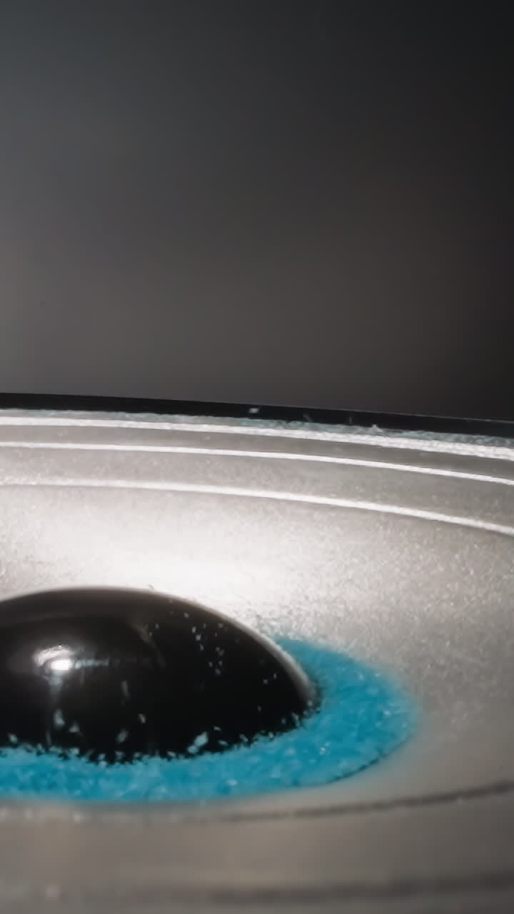 Colored crystalline substance moves from sound vibrations. Blue sand lies near dust cap bouncing under influence of electromagnetic forces on blue background macro