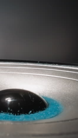 colored crystalline substance moves from sound vibrations. blue sand lies near dust cap bouncing under influence of electromagnetic forces on blue background macro