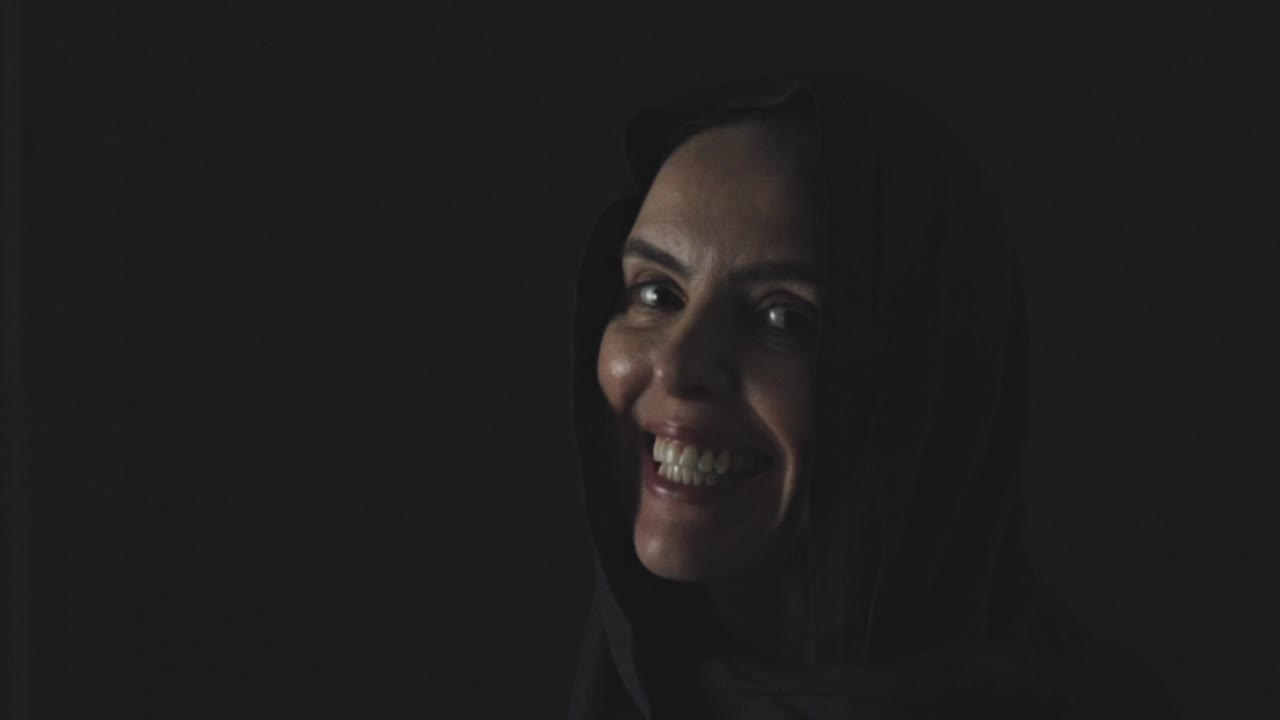 A Muslim woman looks up out of the darkness with a big smile