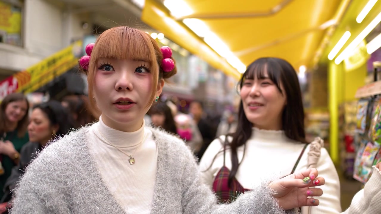 明るい照明が施された活気ある原宿の店で、若い女性たちが色とりどりのスナックの陳列棚を見て回っている。