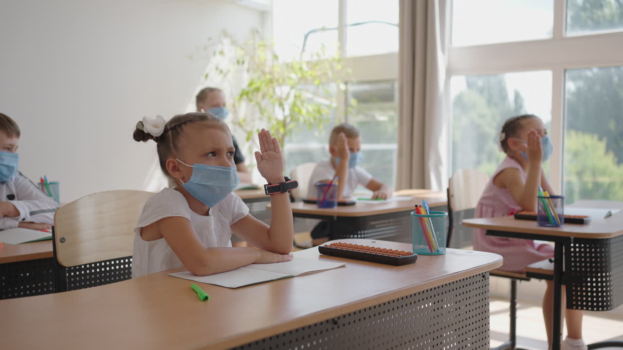 children in the classroom at school in masks sit in the classroom and answer the teacher's questions by raising their hands in slow motion. Lessons during the pandemic at school