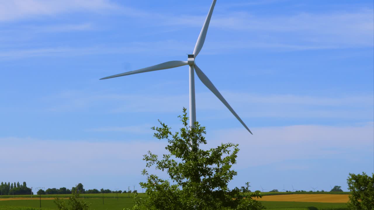 카메라가 회전하는 신재생 에너지 풍력 터빈을 느린 동작으로 포그라운드의 나무와 농장, 과 파란 하늘 4k