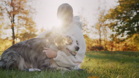 a ten-year-old girl is stroking her dog, sitting in the park on the grass. walking with your beloved pet