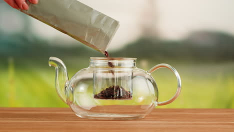 pouring loose leaf tea into a glass teapot