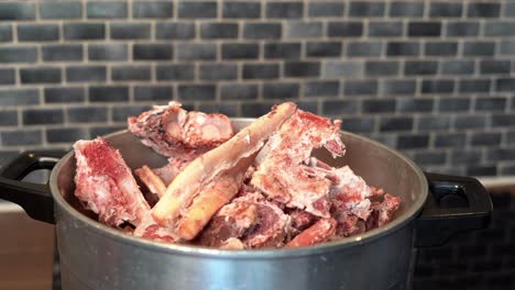 slow-motion heap of raw beef bones falling into kettle on stove