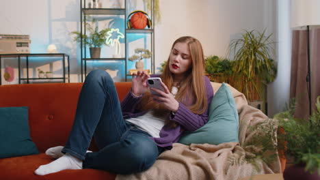 young woman sitting on sofa at home, using smartphone share messages on social media application