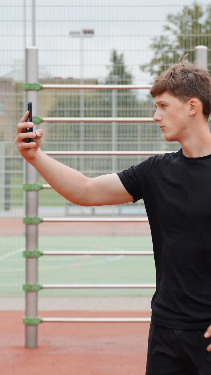 Young man taking selfie outdoors on a tennis court, sporty mood, vertical