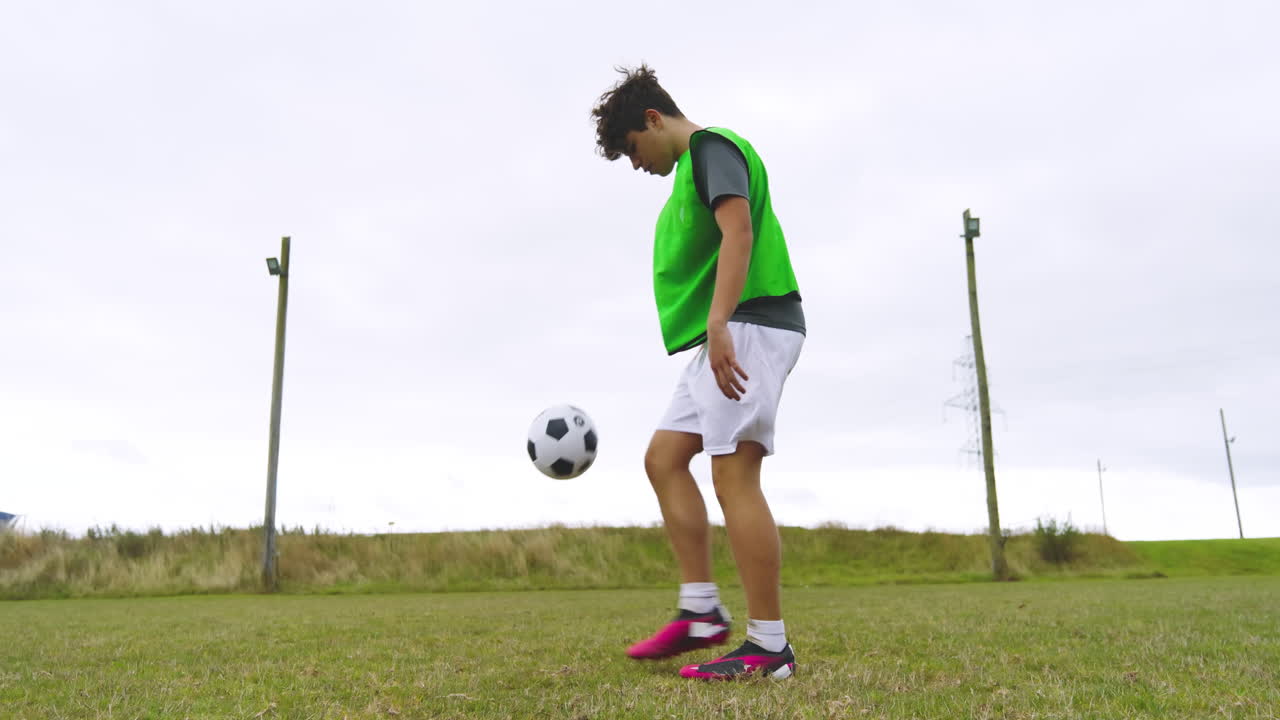 Male soccer player wearing green vest, training, warming up and practicing bouncing ball on pitch