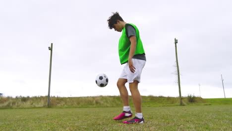 male soccer player wearing green vest, training, warming up and practicing bouncing ball on pitch