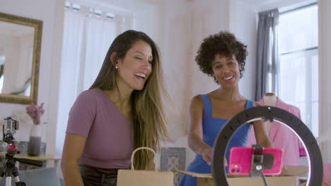 two female friends recording video, unpacking boxes with clothes