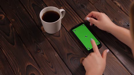 close-up of a woman drinking coffee and using a phone with a green screen.