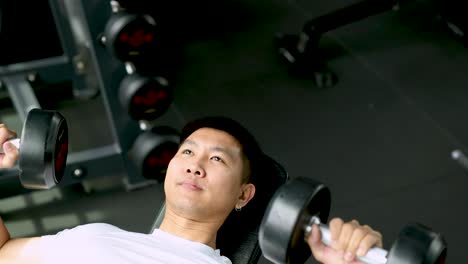 a man exercises with dumbbells on a bench in a well-lit gym, focusing on strength training