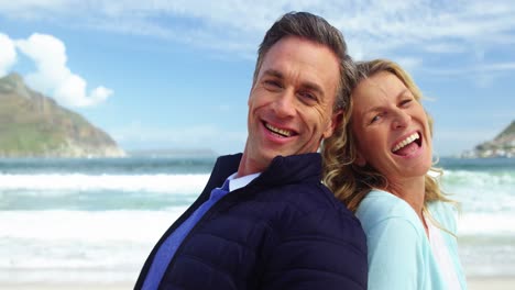 Mature-couple-standing-back-to-back-on-beach