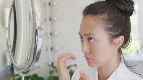 happy asian woman looking at mirror and touching face in bathroom, in slow motion