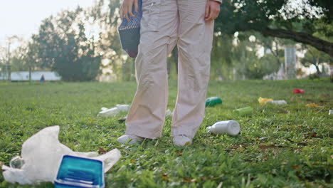 mujer caminando por el césped contaminado en el parque sosteniendo una bolsa ecológica de primer plano. pies de niña