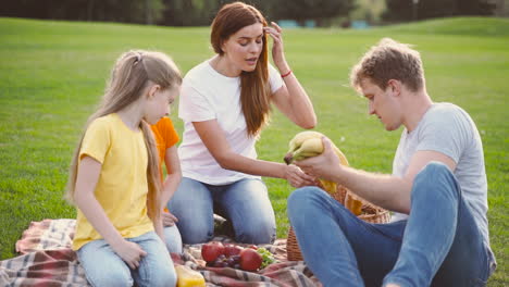 Glückliche-Eltern-Mit-Zwei-Kleinen-Töchtern,-Die-Essen-Aus-Dem-Korb-Nehmen,-Während-Sie-Zusammen-Auf-Der-Grünen-Wiese-Im-Park-Picknicken