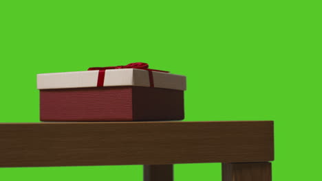 close up of gift wrapped present on table shot against green screen