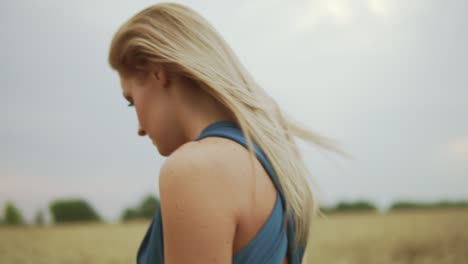 close up view of attractive young blond woman in a blue dress walking through golden wheat field. freedom concept. slow motion