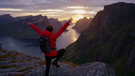 hiker on mountain peak overlooking majestic fjord at sunset