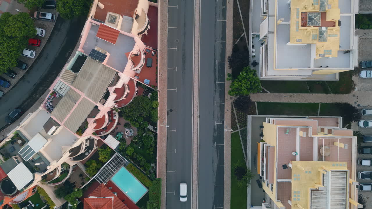 Vista da drone di una strada cittadina con strada asfaltata che corre tra edifici residenziali.