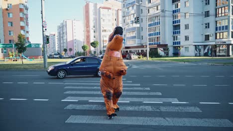 man in dino mascot. person in t rex mascot costume at city street crosswalk
