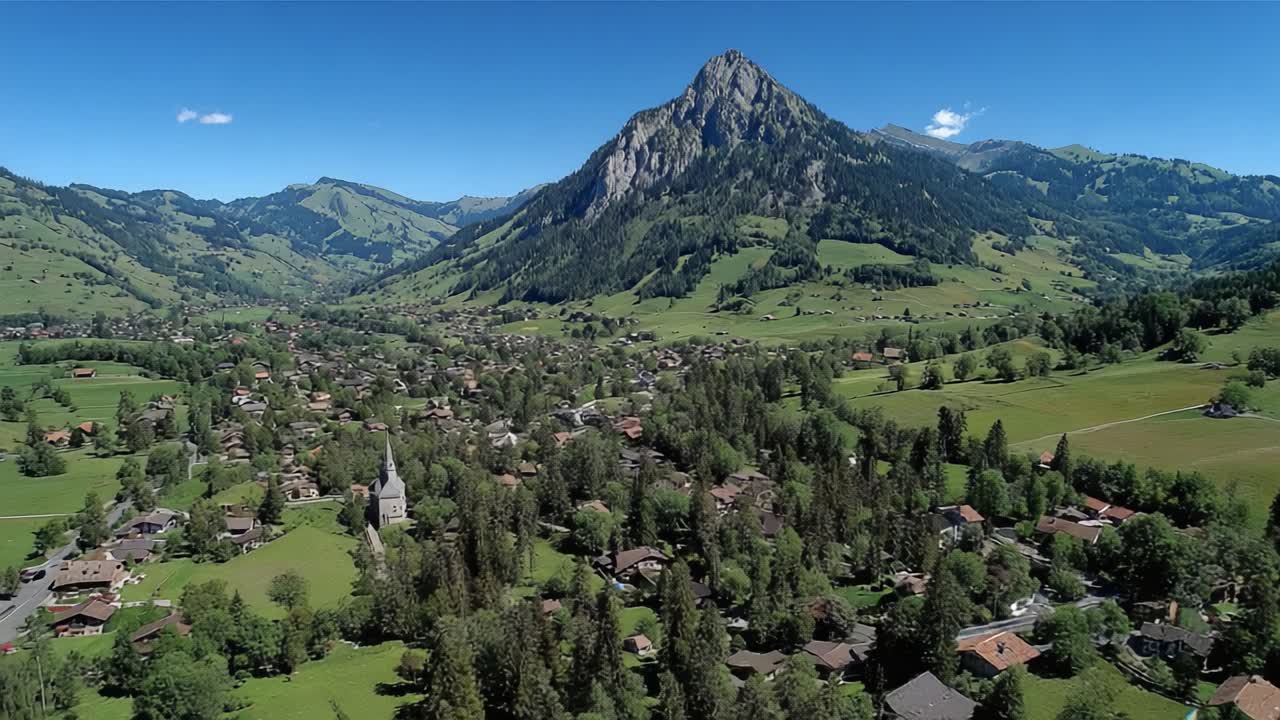Aerial View of Lush Green Valley Surrounded by Majestic Mountains and Charming Village Architecture in Bright Daylight, Showcasing the Beauty of Nature's Landscape