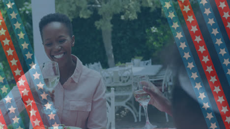 animation of stripes with stars over happy african american women drinking wine in garden