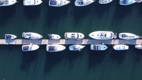 a top down drone shot of a pontoon, flying to the right, with many yachts and motorboats moored up