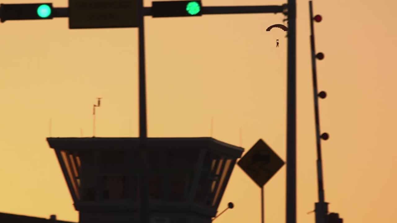 해질녘 하늘에서 낙하산 병사가 전경에서 다리를 건너는 학교 버스와 함께 하늘에서 떨어집니다.