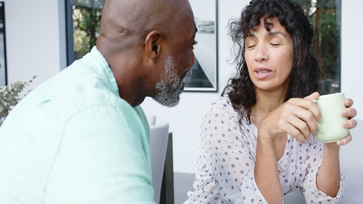 Happy biracial couple having scrambled eggs for breakfast and talking in kitchen, slow motion