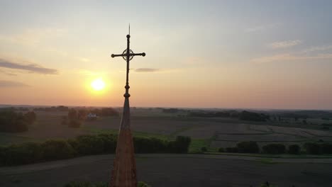 sunset over a church steeple with cross in rural fields