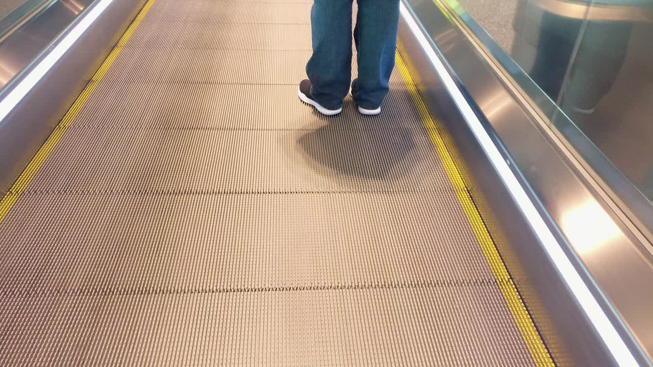 Udsigt til en persons fødder og ben, der står på en rullende gangbro i Bangalore lufthavn, nærbillede, statisk