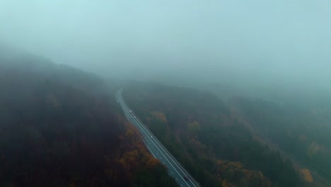 long winding road with passing cars through natural scenery on a cold autumn morning