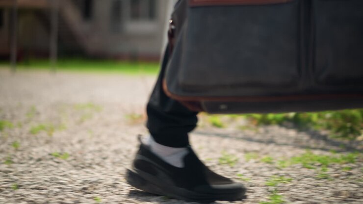 Scarpa da ginnastica sulla ghiaia, passi di scarpe su una superficie pavimentata ruvida, un individuo si avvicina e si ferma in un'area urbana vuota, un primo piano cattura la scarpa da ginnastica che arriva delicatamente su un terreno accidentato nella periferia della città
