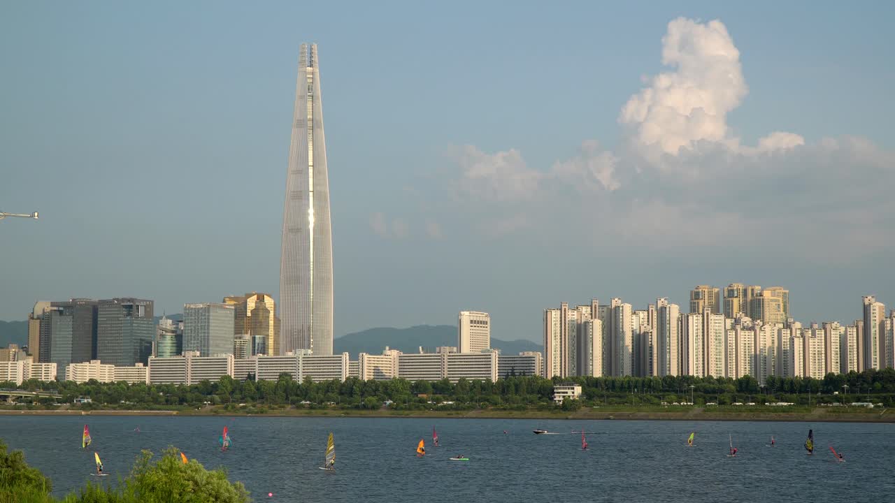 석양을 배경으로 롯데타워를 배경으로 한강에서 윈드서핑하는 사람들