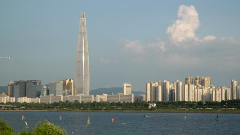 people windsurfing on han river with lotte tower on background at sunset